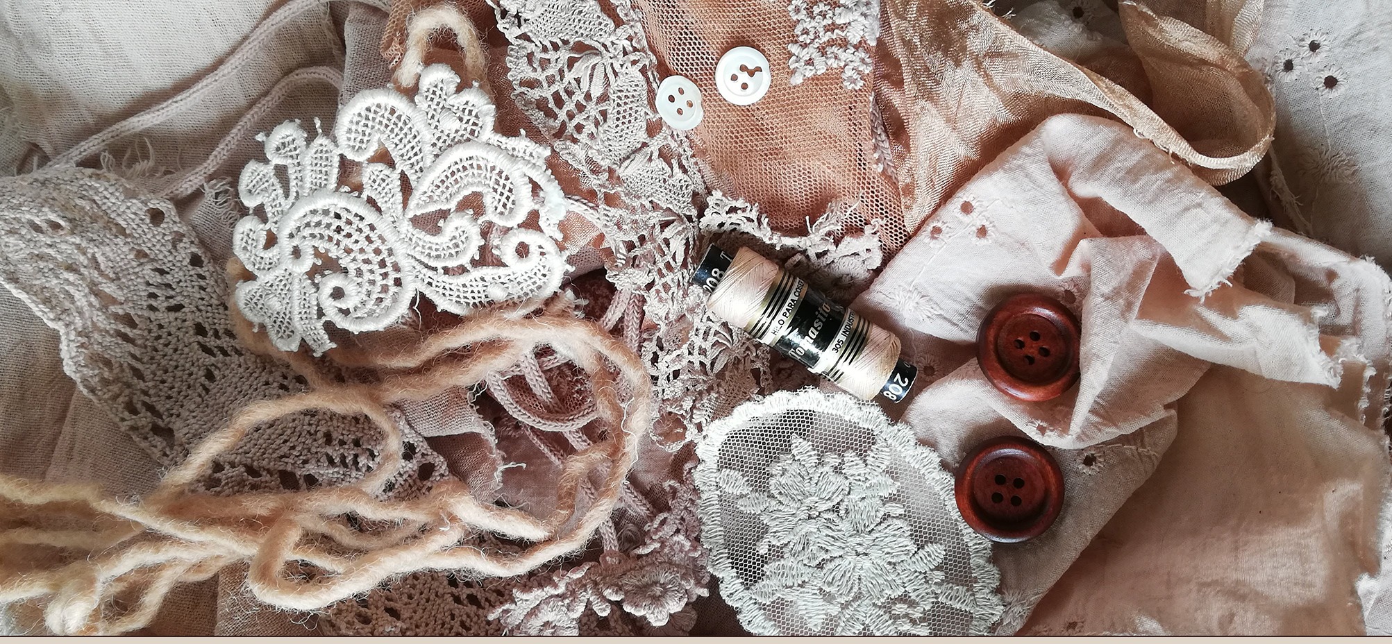 Lace, dusty-rose fabric, wooden buttons, and a spool of thread laid out on a table